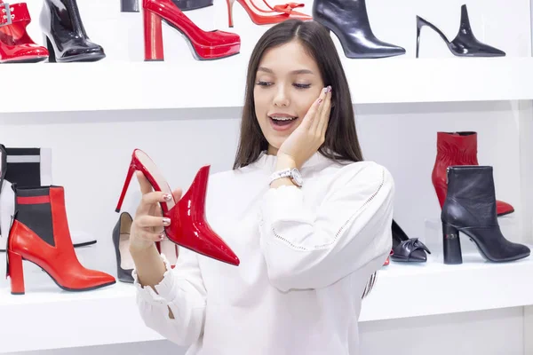 girl buys shoes, a boutique selling shoes. beautiful girl is shopping. on the background of a girl shelves with shoes. Red shoes. the girl has braces on her teeth.