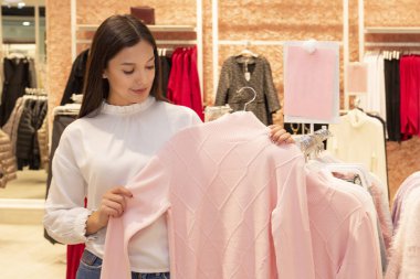 Alışveriş kızı. Uzun siyah saçlı güzel bir kız bir butikte, kendine bir süveter seçiyor. Fiyat etiketlerine bakar ve kalitesini kontrol eder. kopyalama alanı