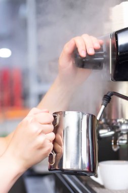 Kahve dükkanı çalışanı buharlı espresso kahve makinesinde kahve hazırlıyor. Kahve makinesiyle barista sütü metal sürahide ısıtıyor. dikey resim