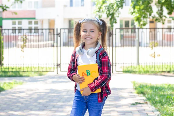 Gelukkig Schoolmeisje Met Een Leerboek Haar Handen Met Hoofdtelefoon Nek — Stockfoto