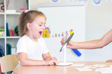 developmental and speech therapy classes with a child-girl. Speech therapy exercises and games with a mirror and cards clipart