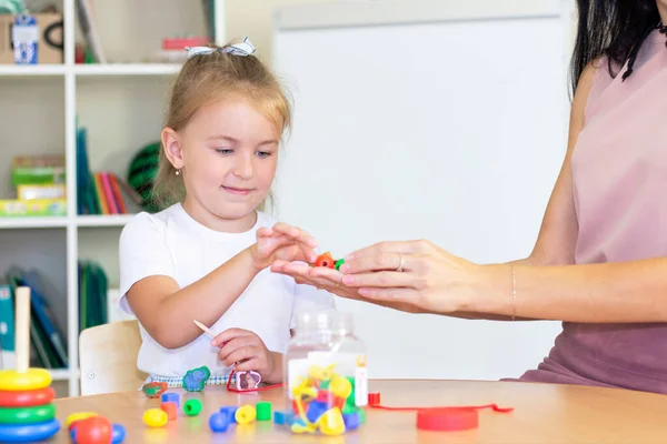 developmental and speech therapy classes with a child-girl. Speech therapy exercises and games with beads. The girl has beads in her hands