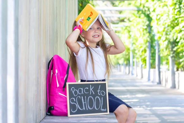 女学生拿着背包和标牌坐着 上面写着要回学校 课本就像你头上的屋顶 — 图库照片