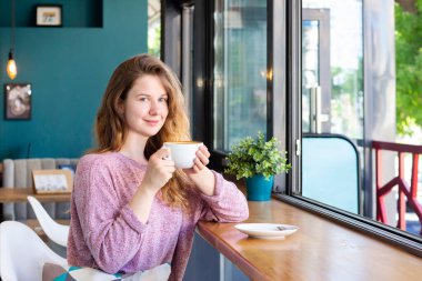 Kafede bir fincan kahveyle gülümseyen ve latte içen bir kız..