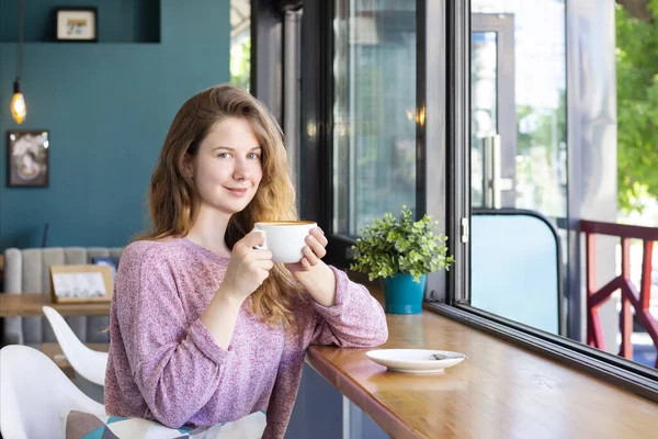 girl in a cafe with a cup of coffee, smiling and drinking a latte.
