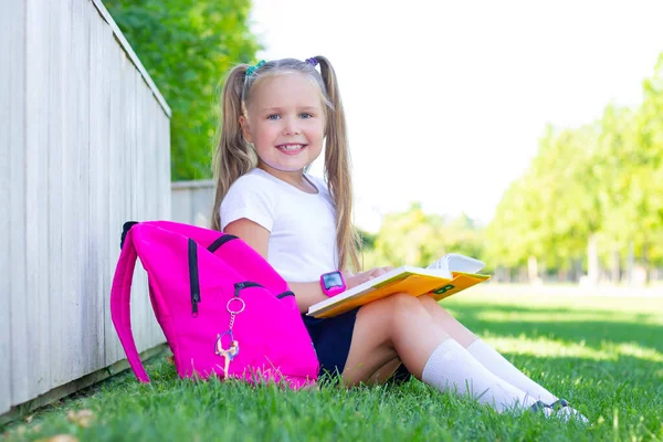 女子高生は草の上にリュックと教科書と笑顔で座り — ストック写真