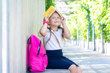 Liseli kız sırt çantasıyla oturuyor. Ders kitabı başınızın üstünde bir çatı gibi