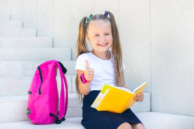 Liseli kız sırt çantası, ders kitabı ve gülücüklerle oturuyor..