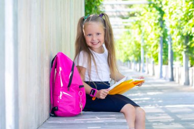 Liseli kız sırt çantası, ders kitabı ve gülücüklerle oturuyor..