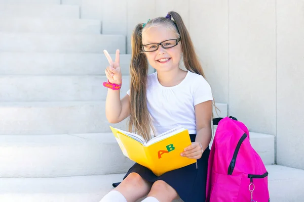 Schoolmeisje Zit Met Een Rugzak Een Leerboek Glimlacht — Stockfoto