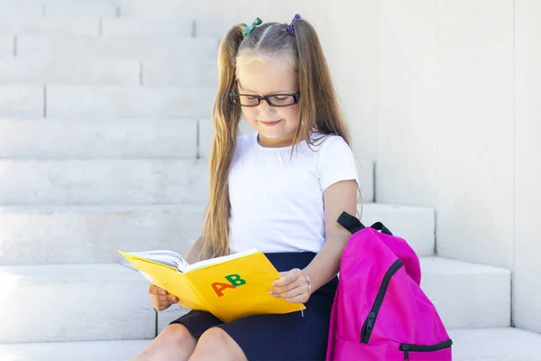 Schoolmeisje Bril Zit Met Een Rugzak Een Leerboek Glimlacht — Stockfoto