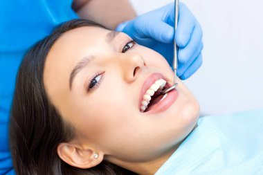 Güzel gülüşü olan genç bir bayan hasta dişçi kliniğinde diş muayenesi yapıyor. Sağlıklı dişler ve ilaçlar, stomatoloji konsepti