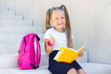 Liseli kız sırt çantası, ders kitabı ve gülücüklerle oturuyor..