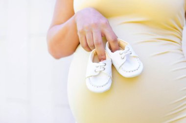 Hamile bir kadının karnındaki doğmamış bebek için küçük ayakkabılar..