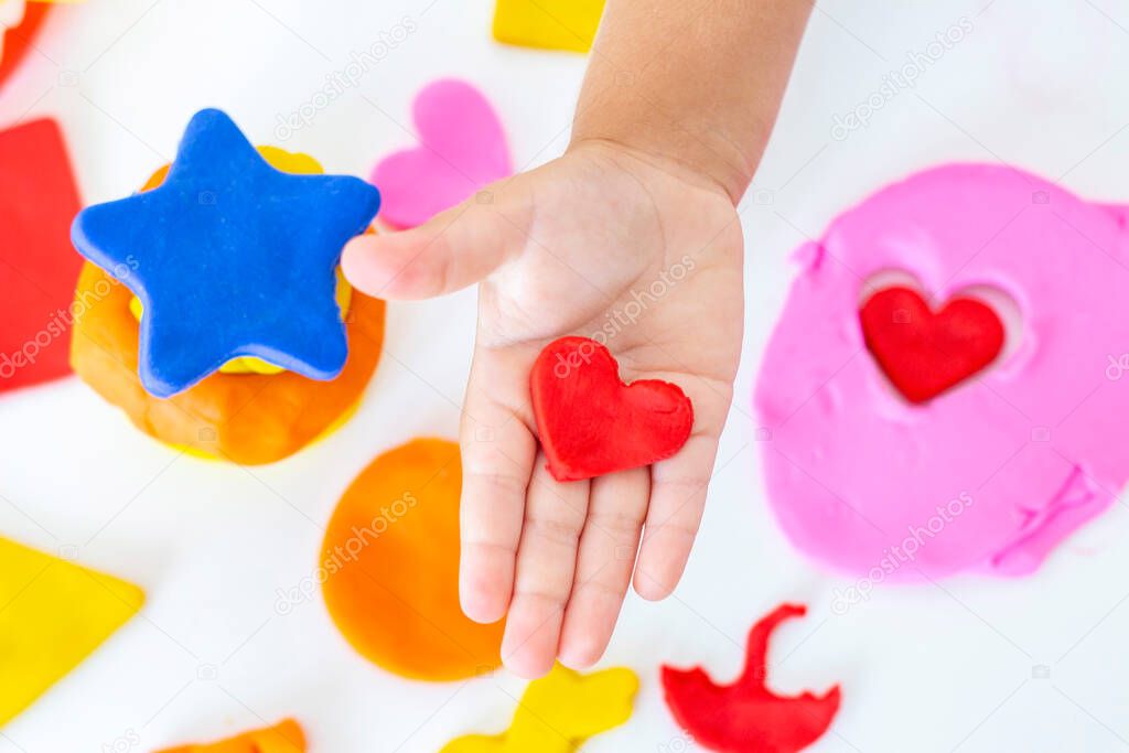Toddler sculpts from colored plasticine on a white table. The hand of a small child squeezes pieces of colored plasticine. Childrens creativity, educational games, fine motor skills. plasticine heart