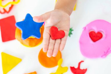Beyaz bir masanın üzerinde renkli plastikçiden bebek heykelleri. Küçük bir çocuğun eli renkli plastiğin parçalarını sıkıyor. Çocukların yaratıcılığı, eğitim oyunları, iyi motor becerileri.