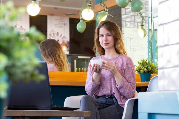 girl works for a laptop. remote work, online. girl in a cafe with a cup of coffee
