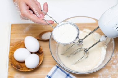 Ekmek ya da ev yapımı hamur işi yapmak. Malzemeler masanın üstünde. Kadın elleri hamuru karıştırmak için mikser tutuyor.