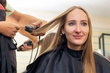 Kadın kuaförü, güzellik salonu. Kuaför saç maşasıyla kıvırcık yapar.