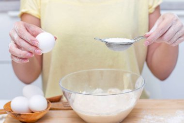 Ekmek ya da ev yapımı hamur işi yapmak. Malzemeler masanın üstünde. Yumurta tutan kadın elleri