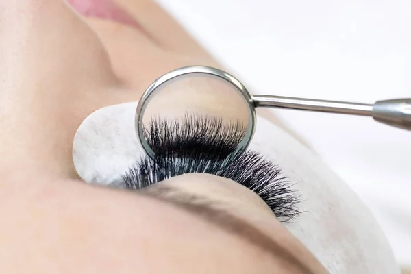 Eyelash extension procedure. Female eye with long eyelashes. Close up. mirror in the hands of the master