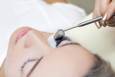 Kirpik uzatma prosedürü. Uzun kirpikli bir kadın gözü. Kapatın. Efendinin ellerinde ayna.