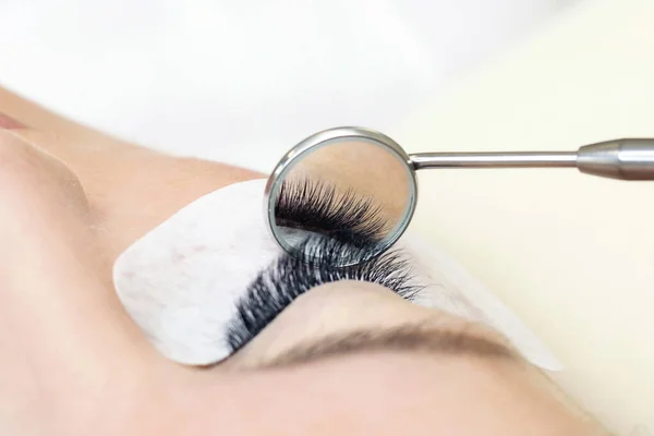 Eyelash extension procedure. Female eye with long eyelashes. Close up. mirror in the hands of the master