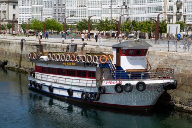 Coruna-Spain.Tourist boat docked in the Coruna dock with the typical galleries of the city in the background on July 7, 2020 clipart