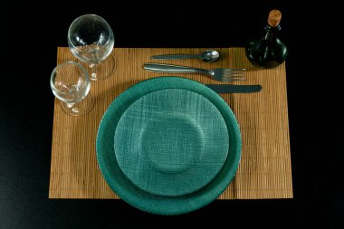 Yeşil plakalı ve yeşil minderli bir masa. Masa çatal, bıçak ve kaşıkla hazırlandı. İki şarap bardağı ve bir şişe şarap var. Sahne zarif ve sofistike.