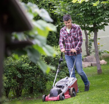Yakışıklı genç adam kesme çim arka bahçesinde Bahar elektrik biçme