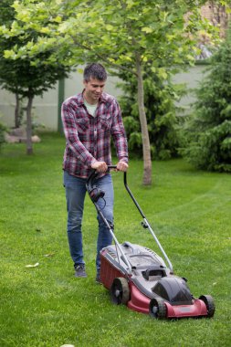 Yakışıklı genç adam kesme çim arka bahçesinde Bahar elektrik biçme