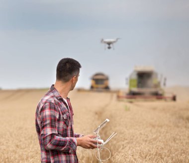 Arkadan Görünüş yakışıklı çiftçinin dron yukarıdaki sürüş elinde uzaktan kumanda ile birleştirmek biçerdöver buğday hasat sırasında
