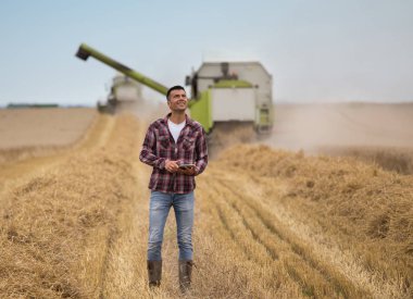 Yakışıklı bir çiftçi hasat alanında sırasında birleştirme hasat önünde tablet ayakta ile gülümseyen