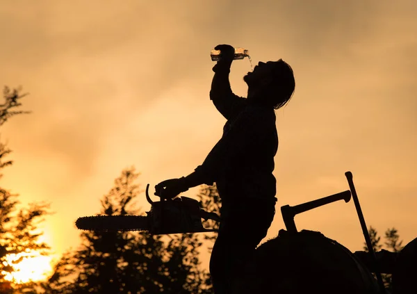 Silueta Leñador Con Motosierra Bebiendo Agua Botella Una Pila Madera — Foto de Stock