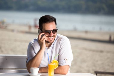 Kafede sahilde oturup, kahve içme ve telefonda konuşurken yakışıklı adam. Zevk sabah Nehri yanında