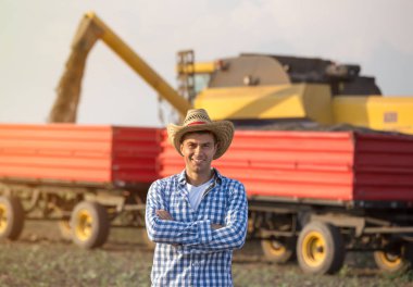 Önünde çapraz kolları olan saman konumu olan yakışıklı bir çiftçi hasat sırasında birleştirmek hasat ve römorklar