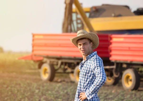 ハンサムな農家の藁に立って収穫中にハーベスタとトレーラーが結合します — ストック写真