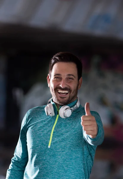 Happy handsome man in sportswear showing thumb up in front of urban colorful background