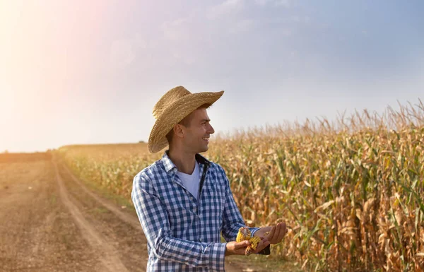 収穫時期のフィールドにトウモロコシの種子を保持している麦わら帽子と笑顔の農家 — ストック写真