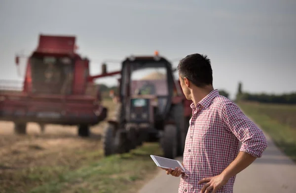 Handsome Farmer Tablet Standing Front Combine Tractor Trailers Field — Stock Photo, Image
