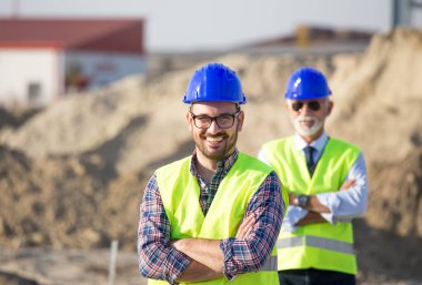 Kask ve site bina yelek ile memnun ve kendine güvenen mühendis portresi