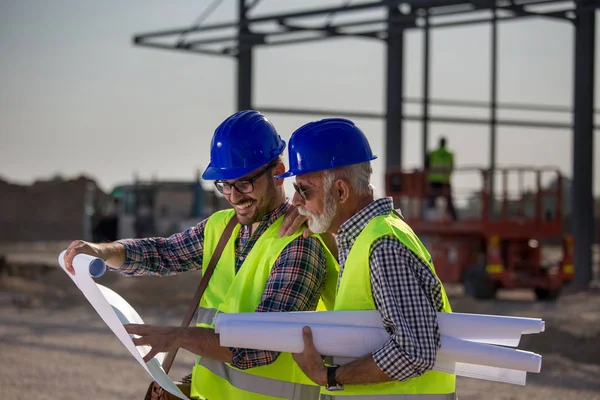 Zwei Zufriedene Ingenieure Betrachten Baupläne Auf Baustelle Mit Metallkonstruktion Hintergrund — Stockfoto