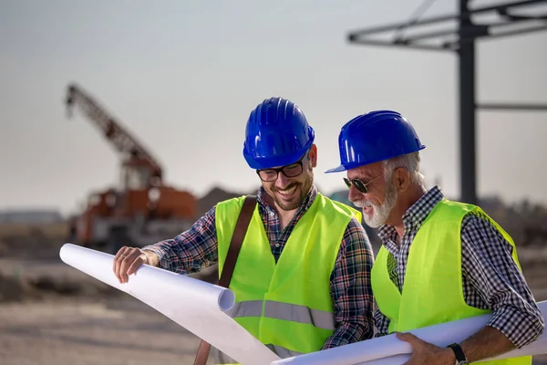 Två Nöjda Ingenjörer Titta Ritningar Byggnadsplatsen Med Metallkonstruktion Bakgrunden — Stockfoto