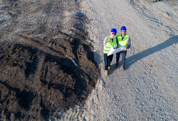 Imagen Aérea Dos Ingenieros Con Cascos Chalecos Sosteniendo Planos Sitio — Foto de Stock