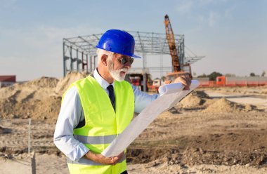 Kıdemli mühendis planları site oluşturma, metal konstrüksiyon önünde bakarak 