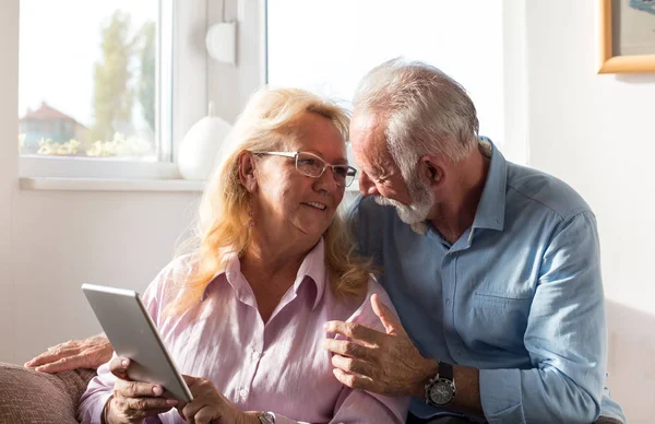 快乐的老夫妇坐在客厅的沙发上看平板电脑 — 图库照片