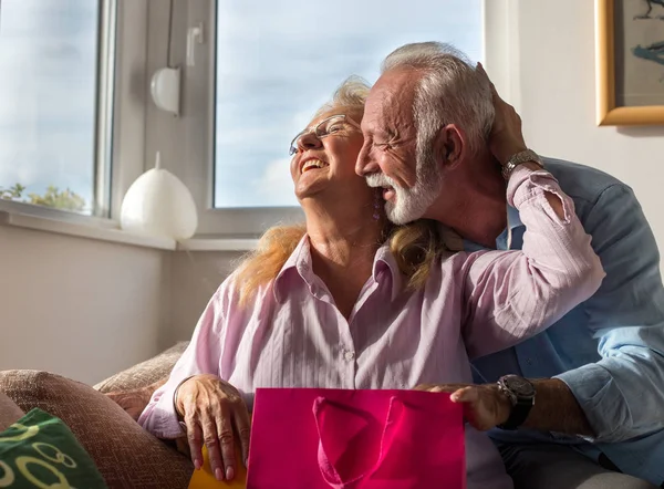 Elderly man giving presents in shopping bags to happy wife