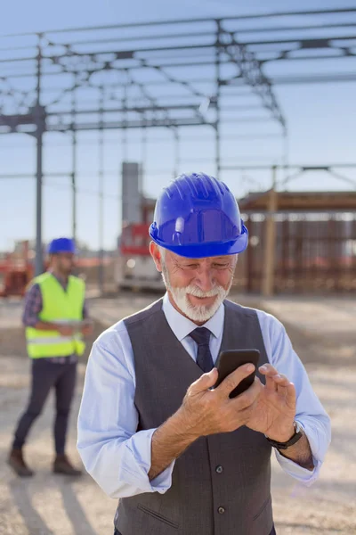 Senior Ingenieur Mit Helm Tippt Auf Handy Auf Baustelle — Stockfoto