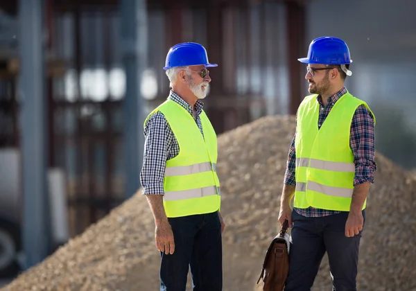 Twee Ingenieurs Met Helmen Vesten Praten Bouwplaats Voor Metalen Constructie — Stockfoto