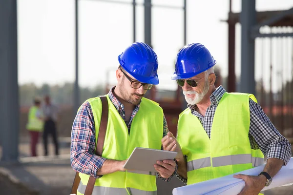 Zwei Zufriedene Ingenieure Betrachten Baupläne Auf Baustelle Mit Metallkonstruktion Hintergrund — Stockfoto